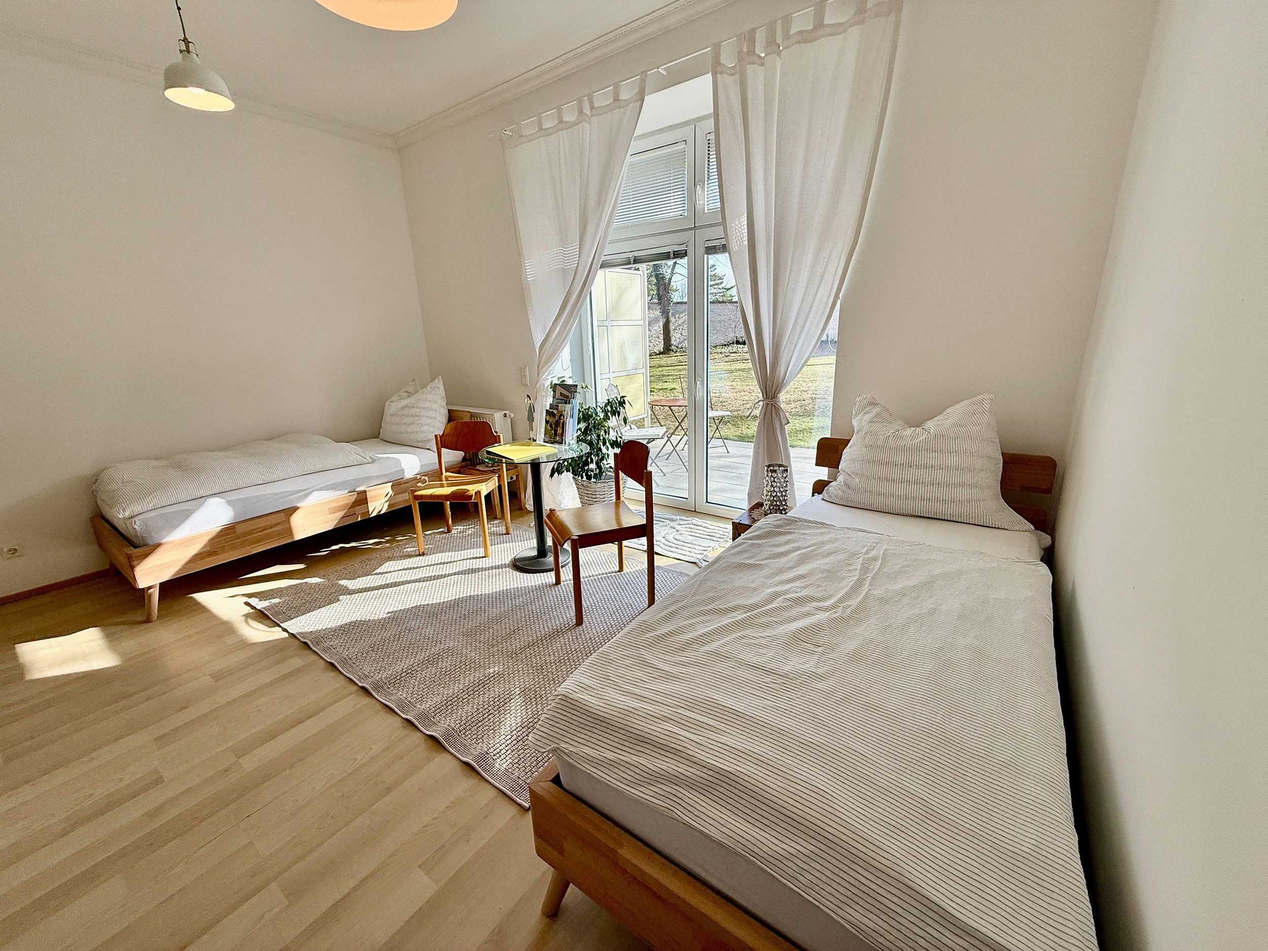 Ein Schlafzimmer mit zwei Betten, einem Tisch, Stühlen und einem großen Fenster mit Vorhängen.