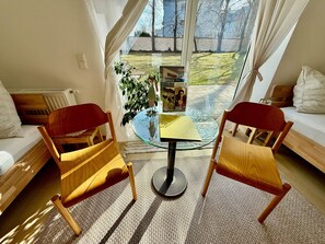 Ein Wohnzimmer mit zwei Holzstühlen, einem Glastisch, einer Couch und Blick ins Freie.