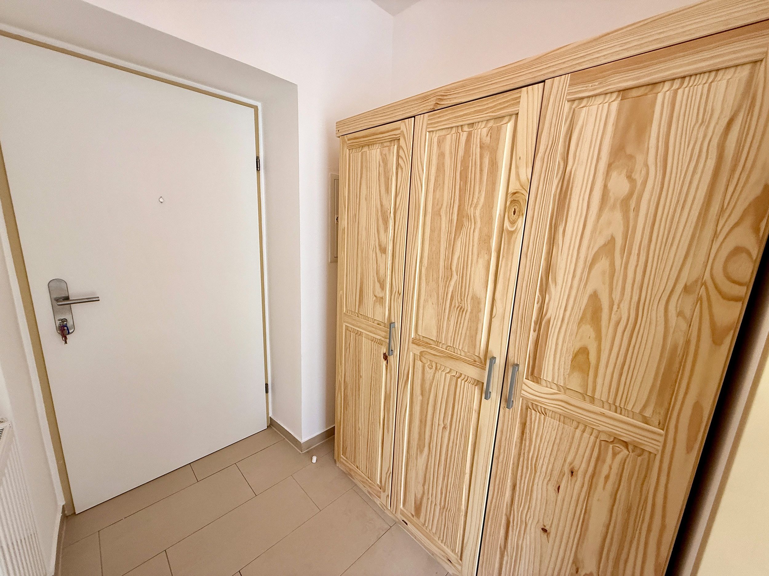 Ein Zimmer mit einer weißen Tür, einem Holfischschrank mit vielen Türen und einem Fliesenboden.