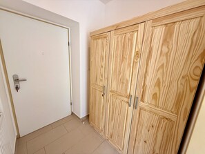 Huone, jossa on valkoinen ovi, useita ovia sisältävä puinen vaatekaappi ja laatoitettu lattia.