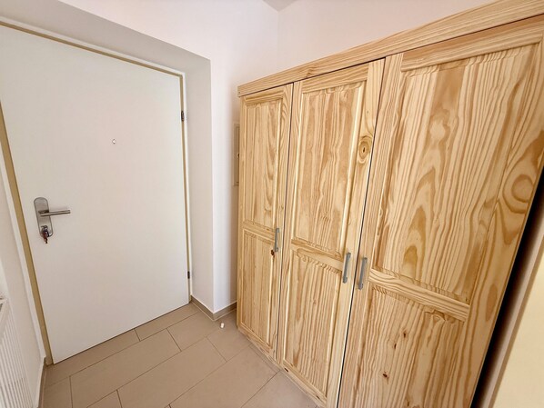 Habitació amb una porta blanca, un armari de fusta amb diverses portes i un sòl de rajola.