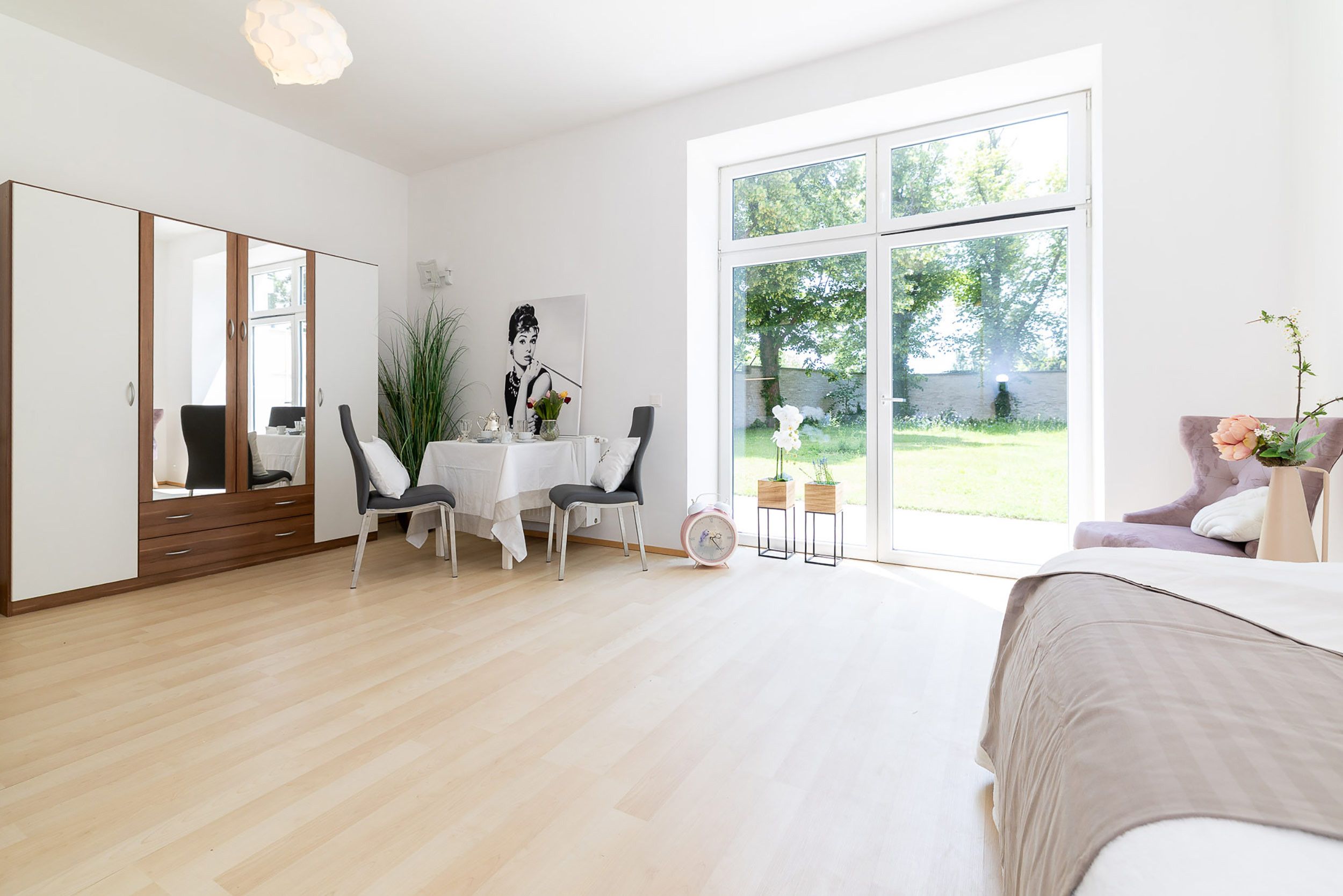 Ein modernes Schlafzimmer mit großem Fenster, einem Bett, einem Schreibtisch mit Stühlen und einem Kleiderschrank.