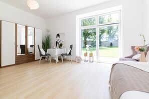 Ein modernes Schlafzimmer mit großem Fenster, einem Bett, einem Schreibtisch mit Stühlen und einem Kleiderschrank.