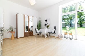 Ein stilvolles Esszimmer mit Holzboden, einem weißen Tisch und Stühlen. Ein großes Fenster bietet Blick auf die grüne Umgebung.