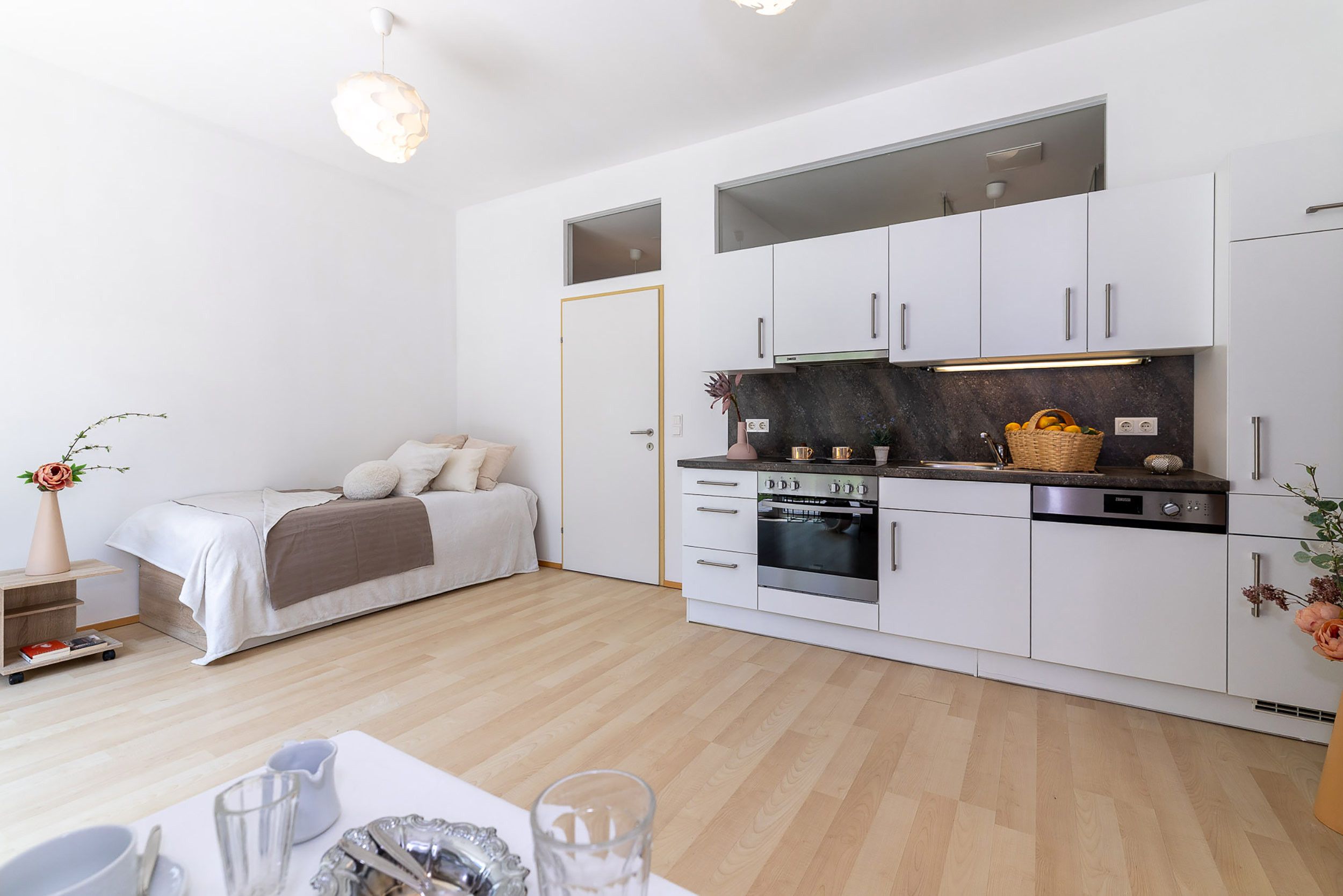 Eine kompakte, moderne Küche mit weißen Schränken, einem eingebauten Backofen und einer Arbeitsplatte mit Obstkorb.