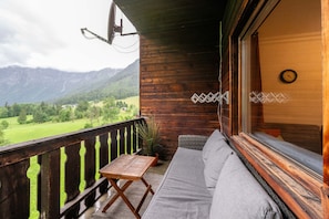 Ein Holzbalkon mit einer Couch und einem Tisch, mit Blick auf eine grüne Landschaft und Berge.