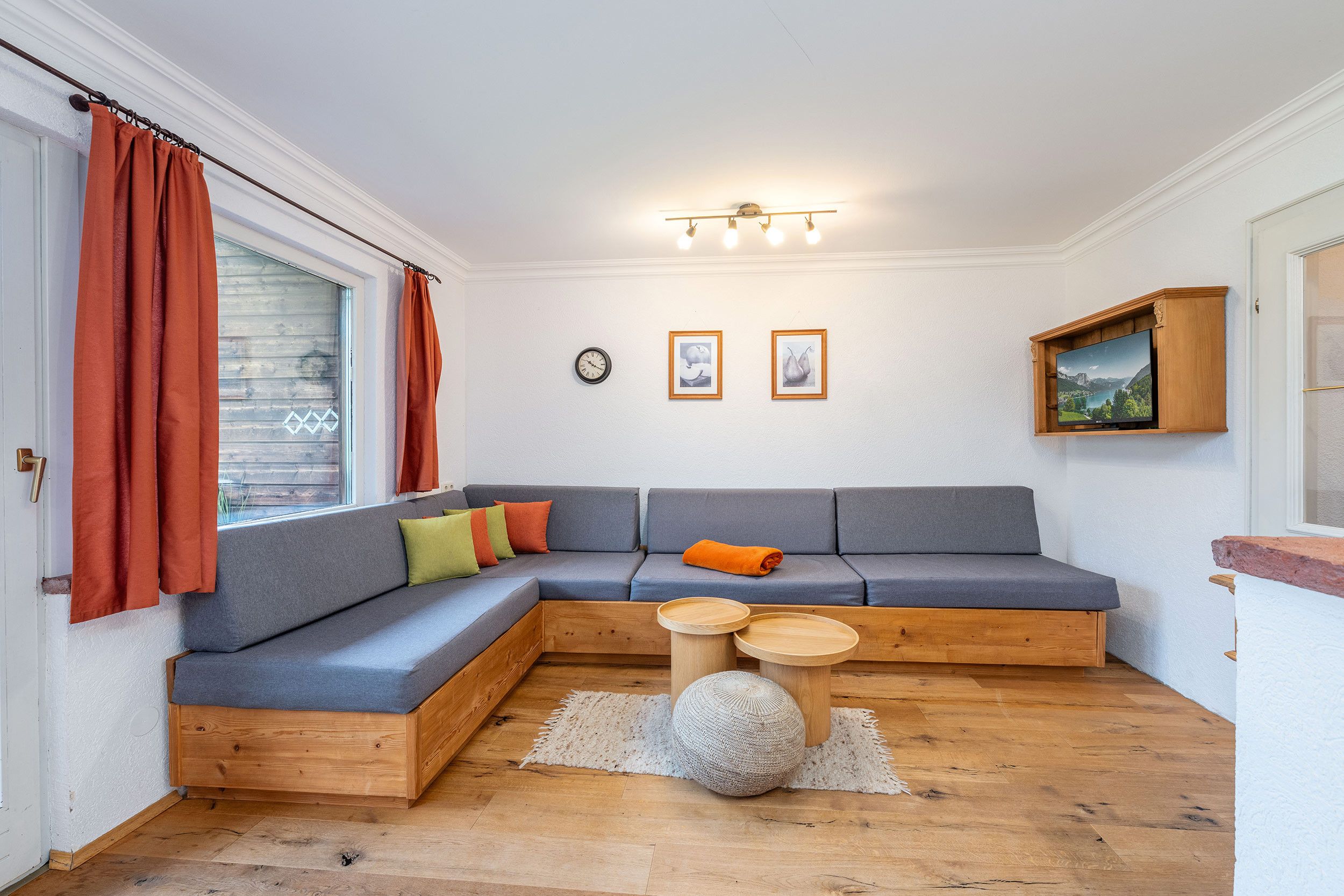 A cozy living room with a sectional sofa, a wooden coffee table, and a large window with curtains.
