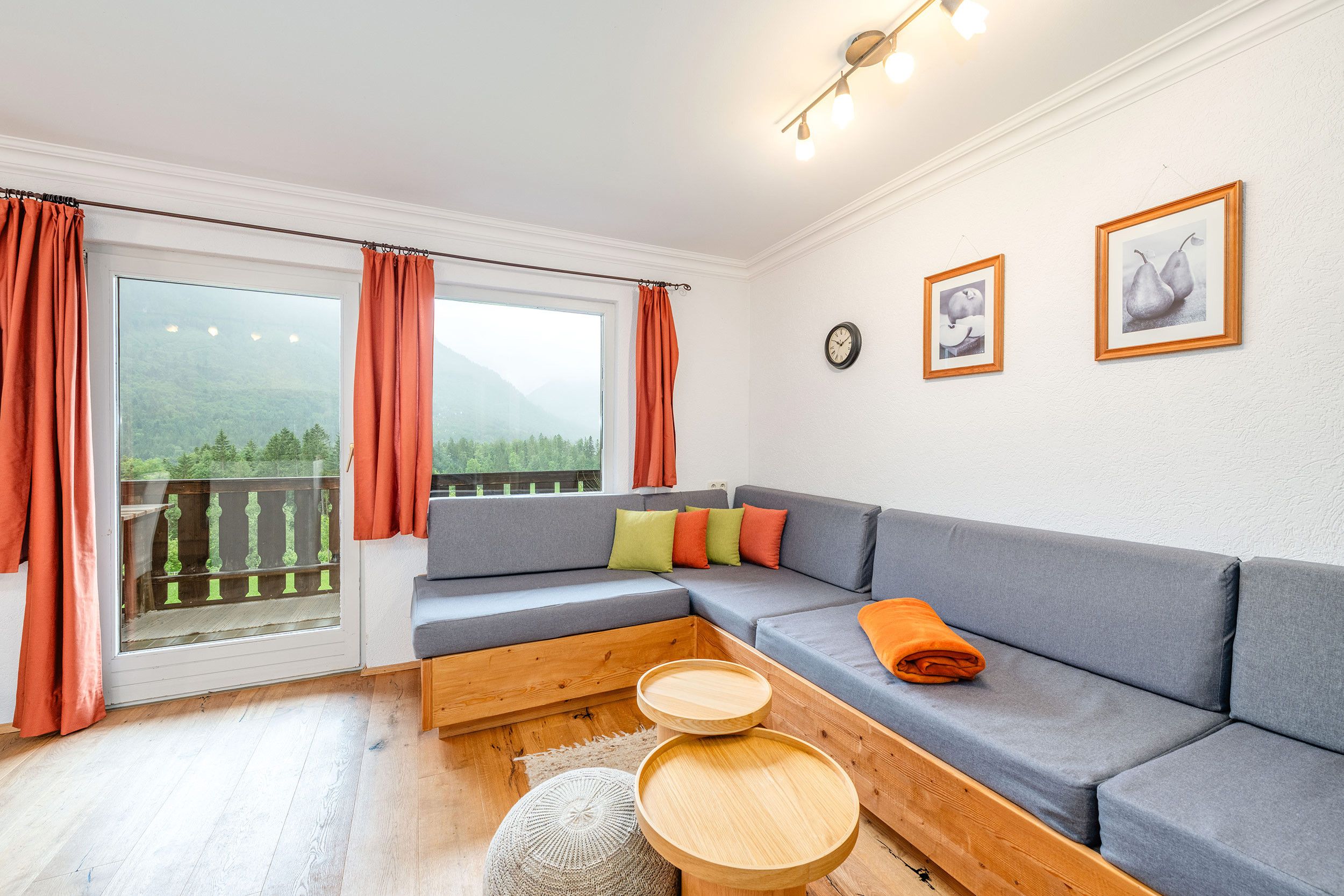 Un soggiorno moderno con un divano grigio, tavolini in legno e un balcone con tende arancioni.