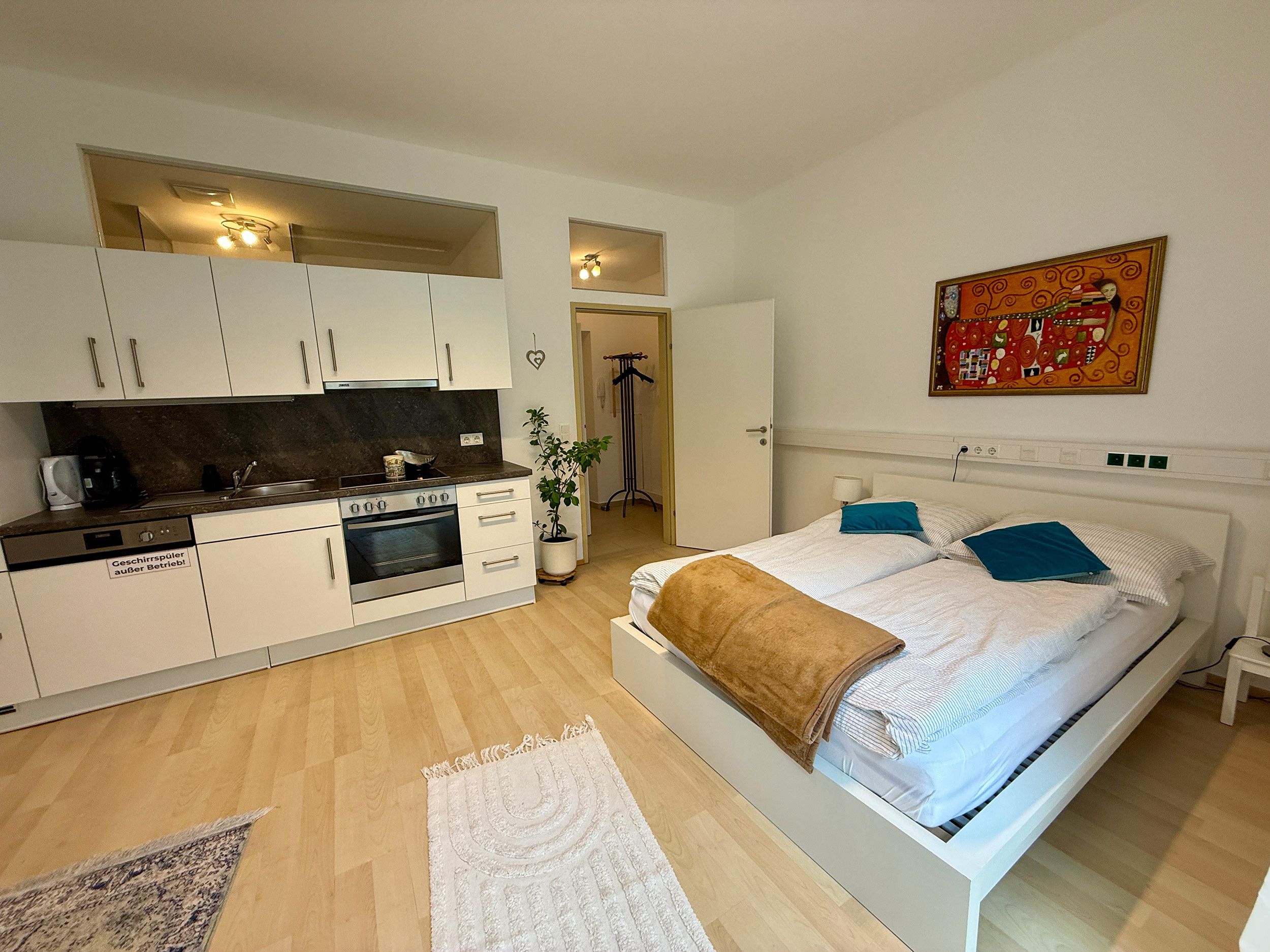 Ein gemütliches Schlafzimmer mit Bett, Nachttischen, einem Fenster und einer Küchenzeile mit Herd und Backofen.