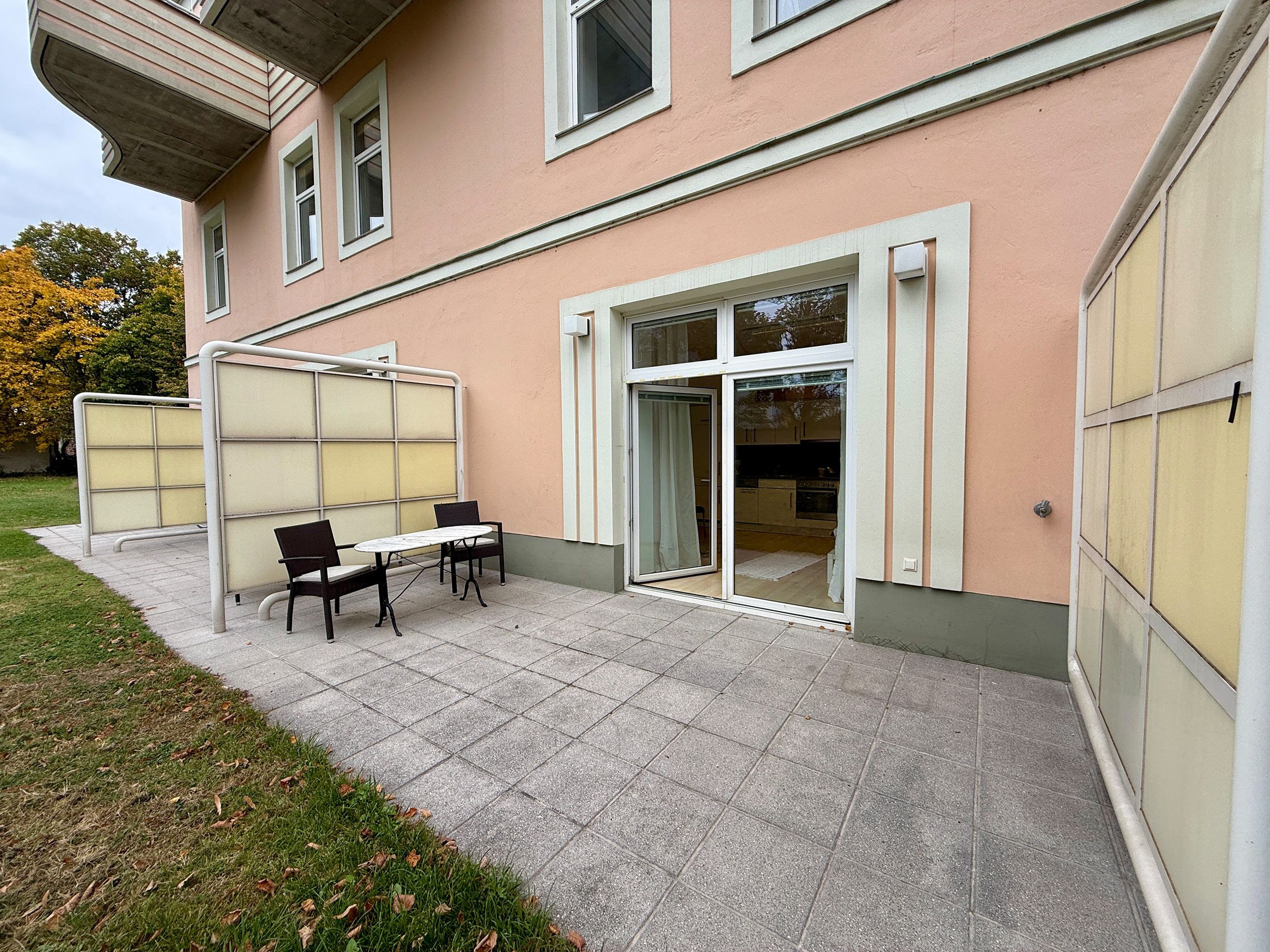 Ein Gebäude mit einer Terrassenfläche, ausgestattet mit einem Tisch und Stühlen, einer Glastür und Blick ins Innere.