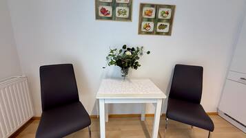Ein Zimmer mit zwei schwarzen Stühlen, einem weißen Tisch und einer Vase mit Blumen. An der Wand befinden sich gerahmte Bilder.