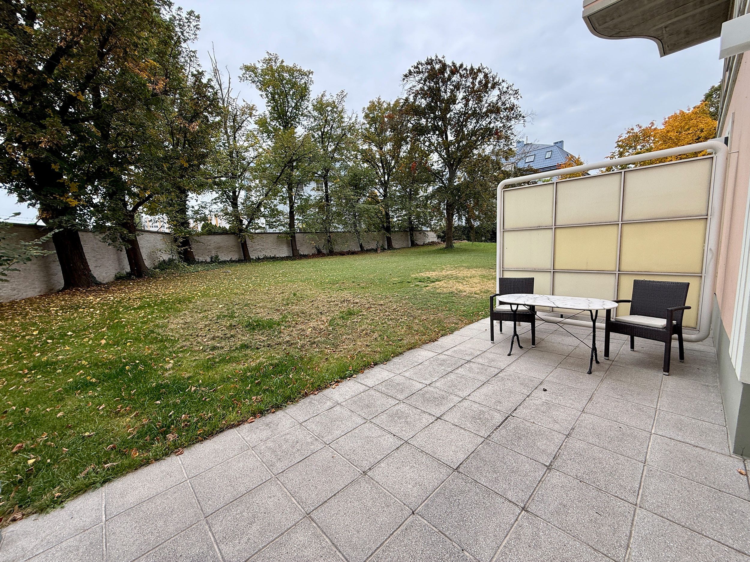 Eine Terrasse mit Tisch und Stühlen, eine Rasenfläche und Bäume.