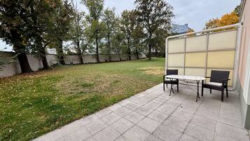 Eine Terrasse mit Tisch und Stühlen, eine Rasenfläche und Bäume.