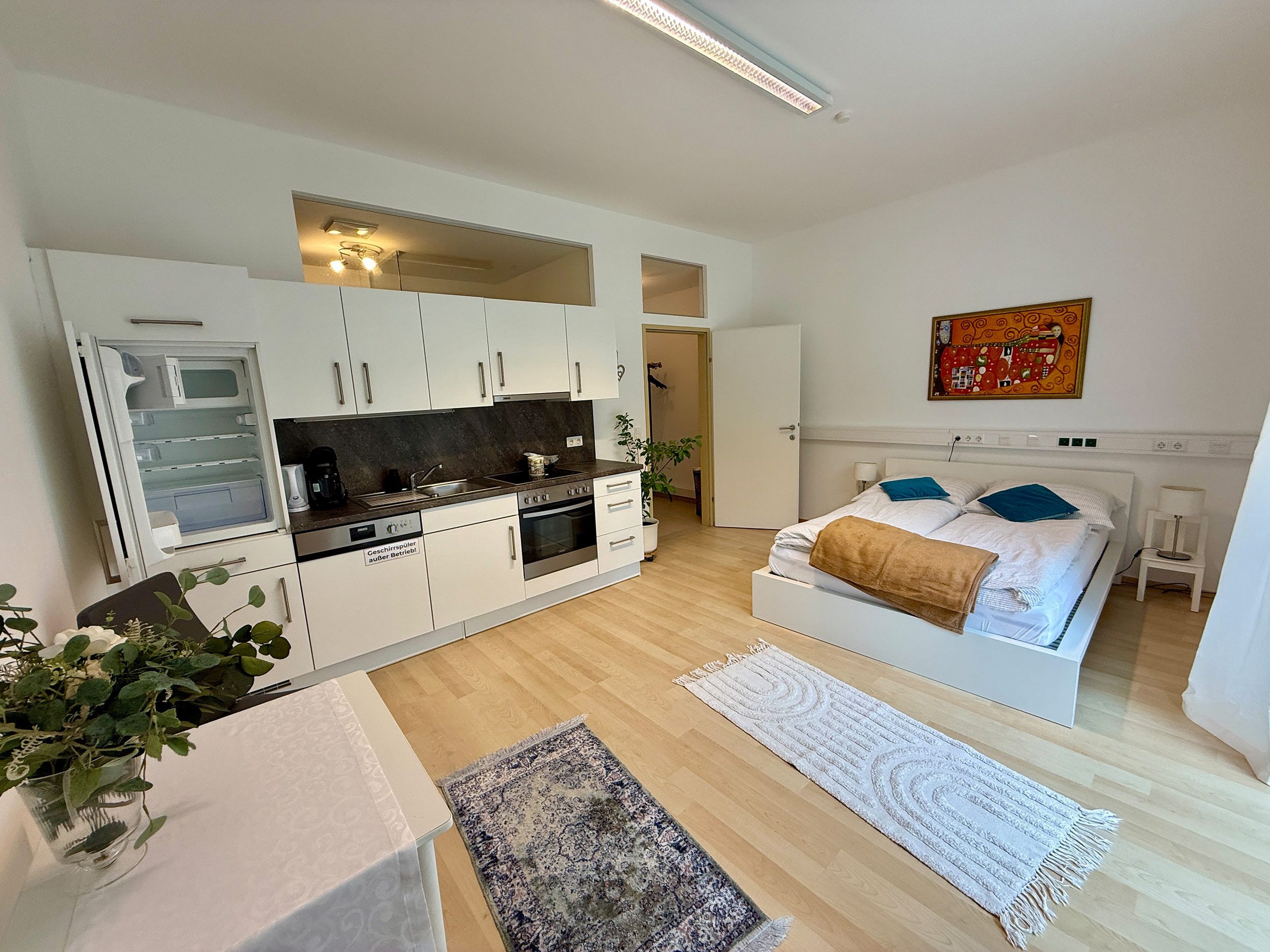 Ein kompakter Wohnraum mit Küchenzeile, einem Bett mit Kopfteil und einem kleinen Nachttisch.