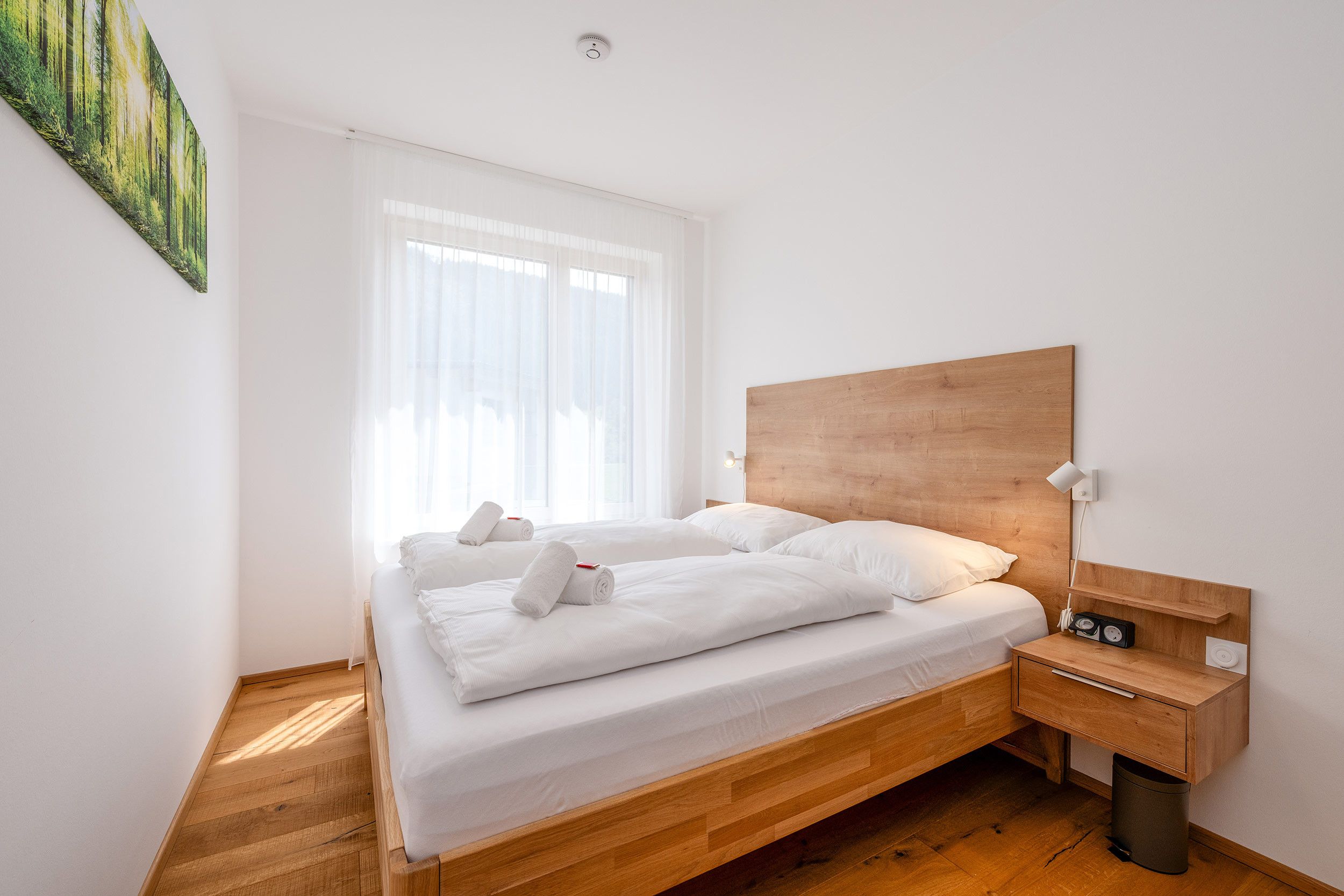 A modern bedroom with a wooden bed frame, white bedding, and a bedside table with a lamp.
