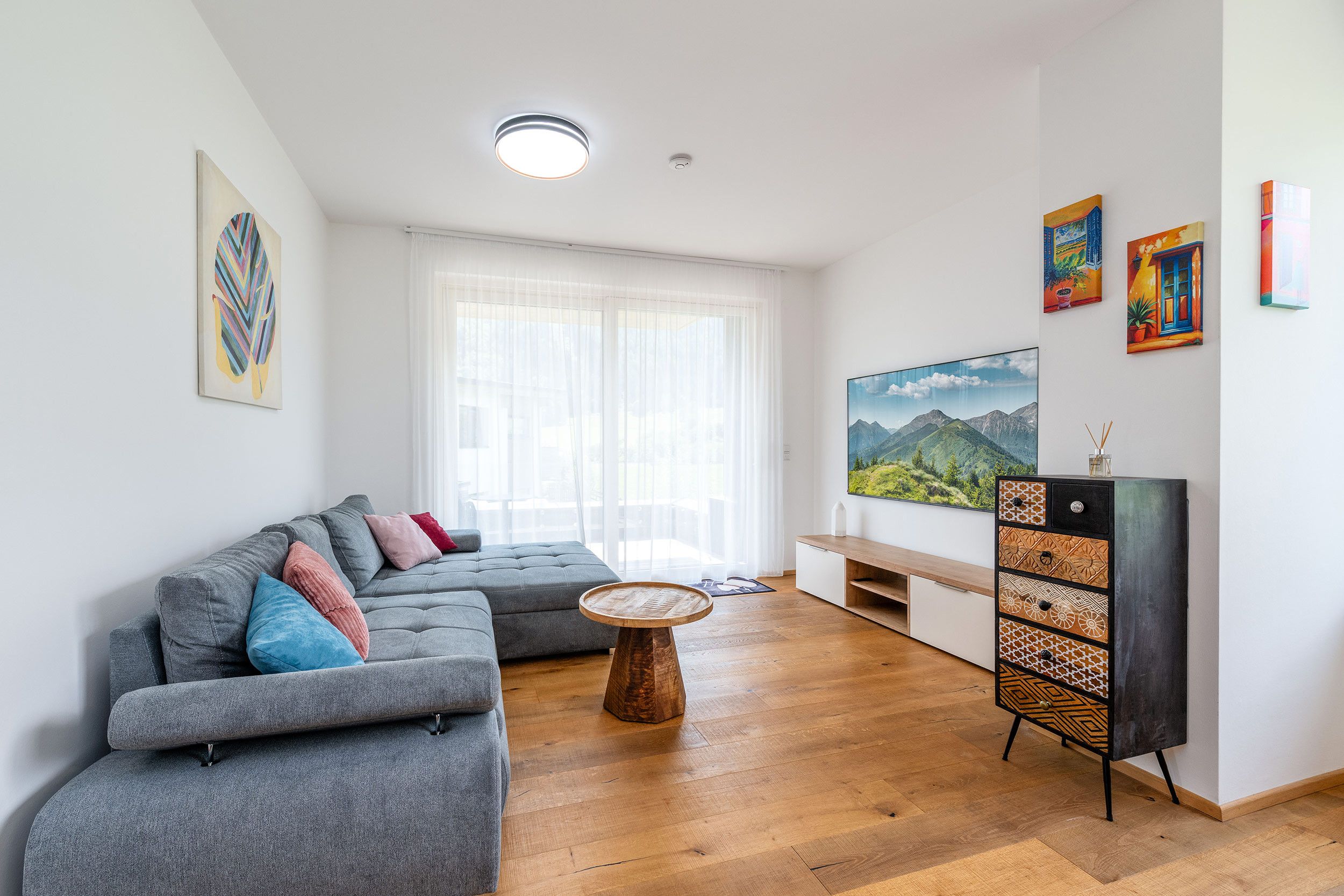 Een moderne woonkamer met een grijze modulaire bank, een houten salontafel en een flatscreen televisie aan de muur.