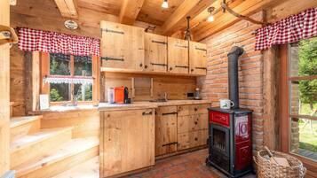 Une cuisine rustique avec des meubles de cuisine en bois, un poêle rouge et noir et un lambrequin à carreaux.