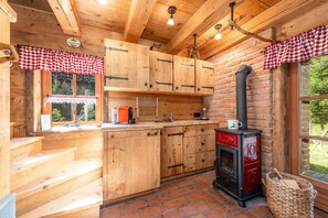 Eine rustikale Küche mit Holzausbau, einem roten und schwarzen Herd und einem karierten Fensterrollo.