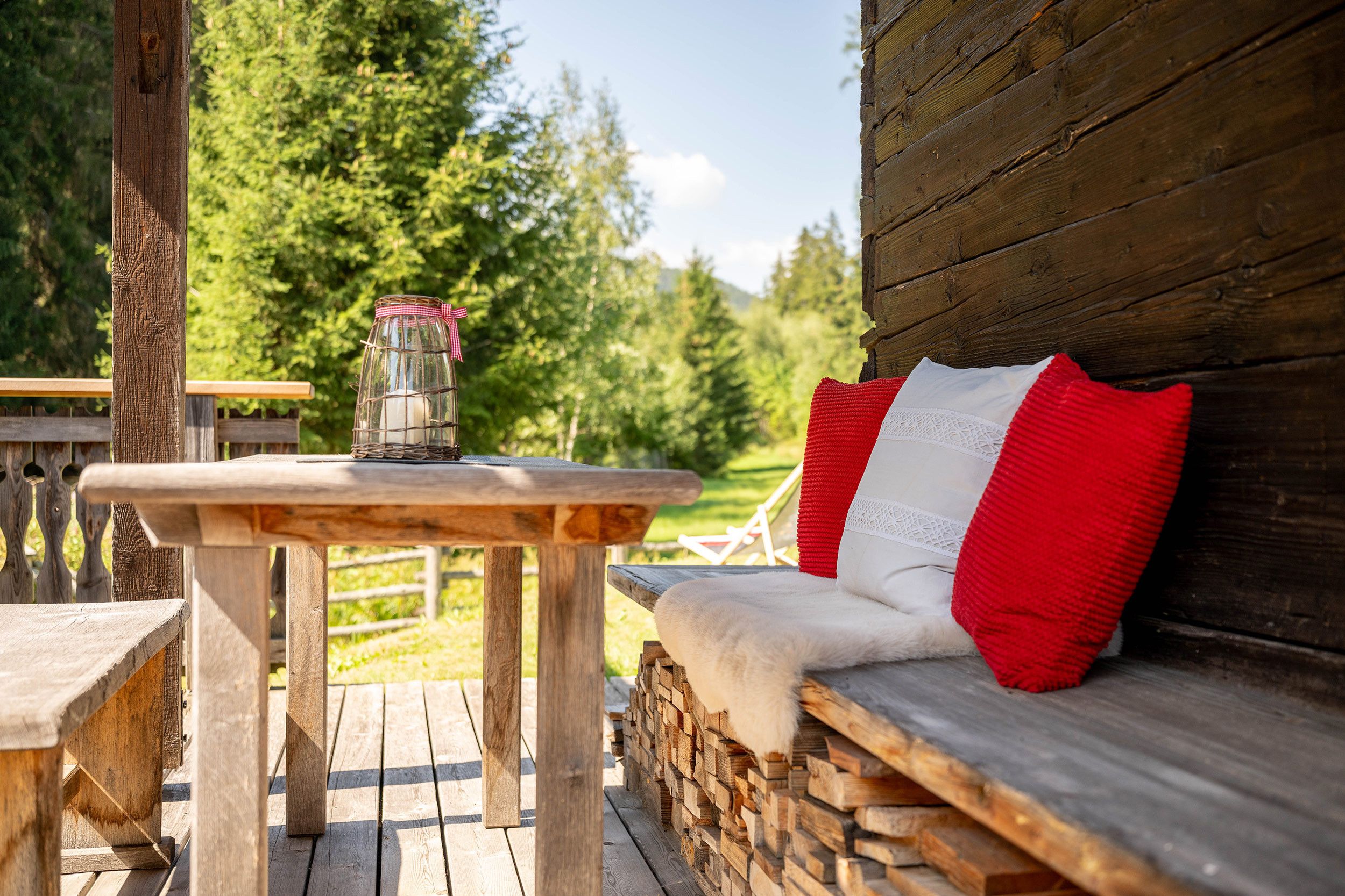 Une terrasse en bois avec une table et un banc agrémenté d’un coussin rouge.