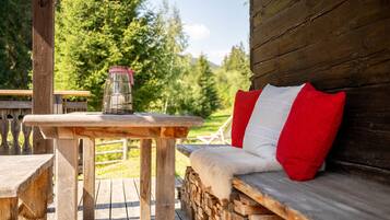 Une terrasse en bois avec une table et un banc agrémenté d’un coussin rouge.