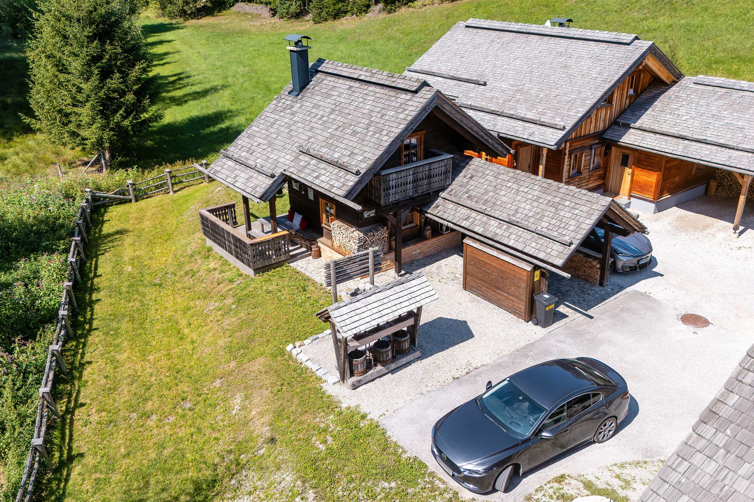 Eine zweistöckige Blockhütte mit Carport und einer kleinen Sitzgelegenheit im Freien.