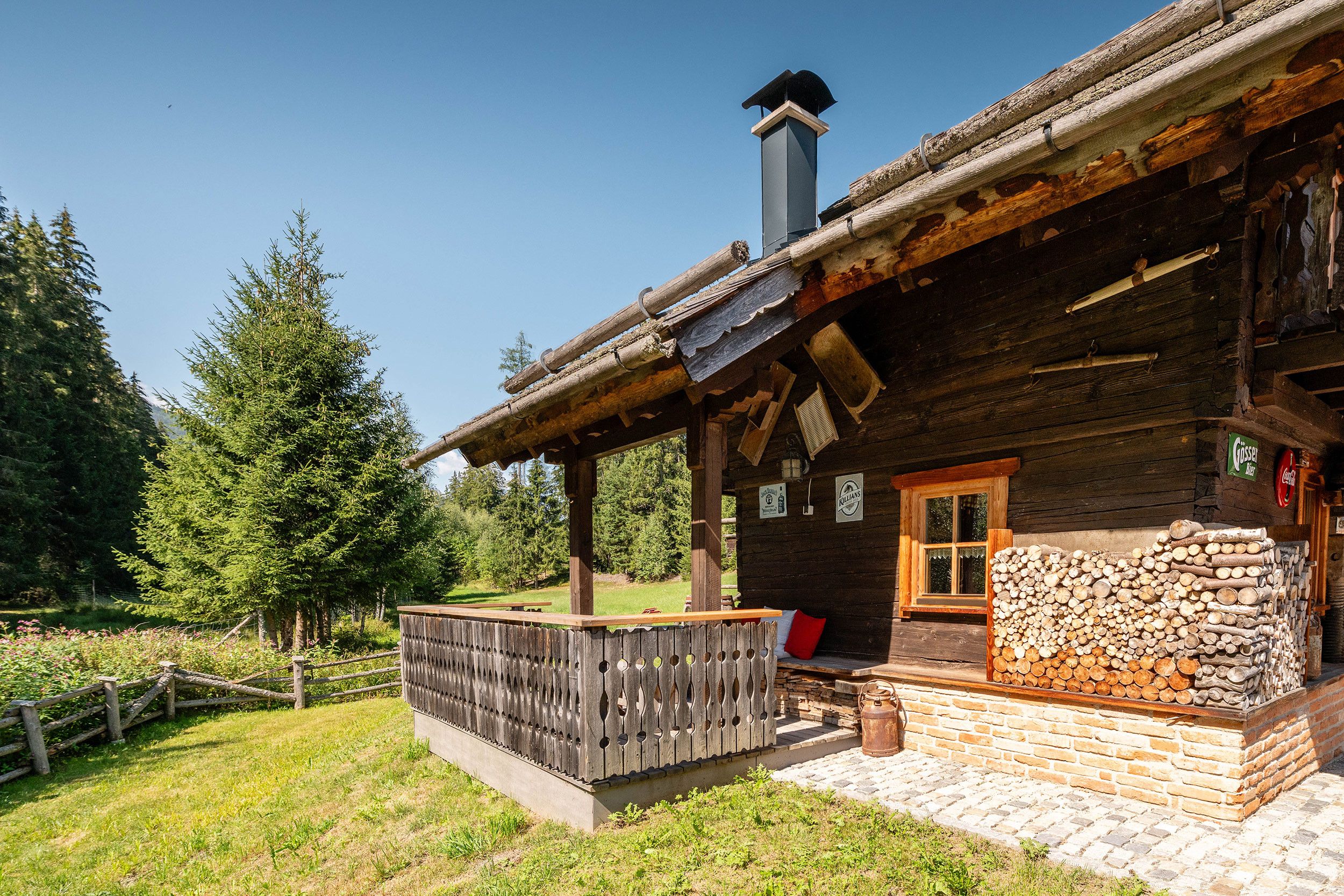 A rustic wooden cabin with a chimney, a wooden deck, and a stack of firewood outside.