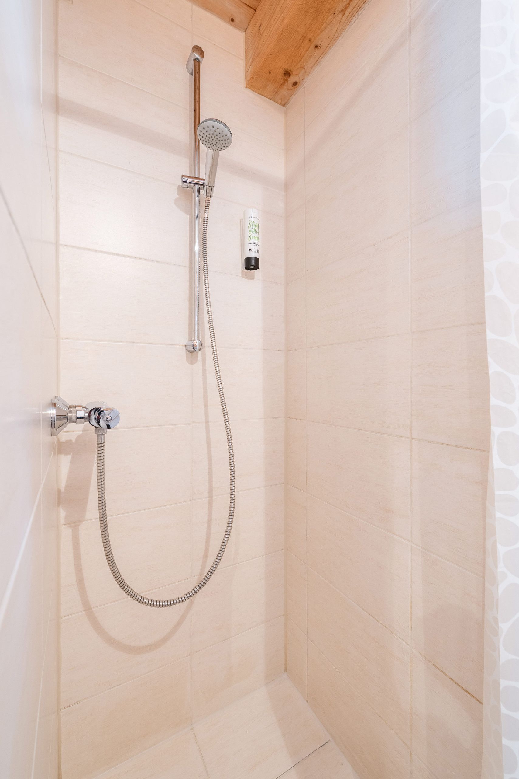 Eine Dusche mit Handbrause, Duschwand und Wandarmatur.