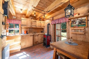 A rustic kitchen with wooden cabinets, a red stove, and a checkered window valance.