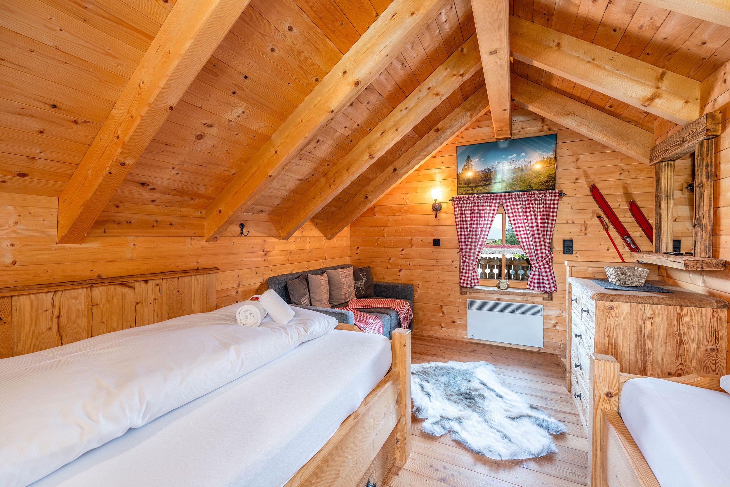 A cozy wooden cabin interior with two single beds, a sofa, a fireplace, and a ski rack.