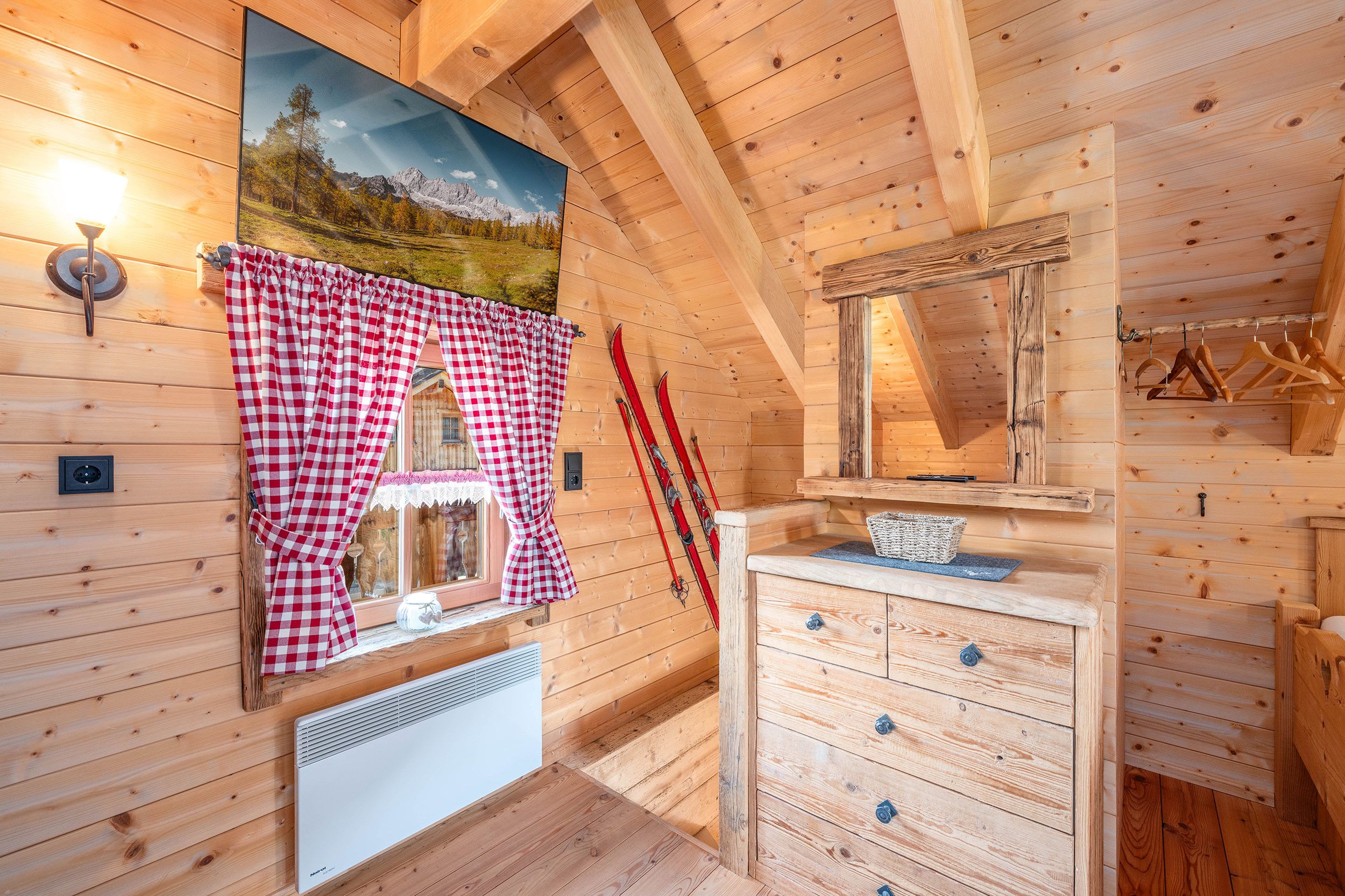 A wooden cabin interior with a checkered curtain, a radiator, a mirror, and ski equipment.