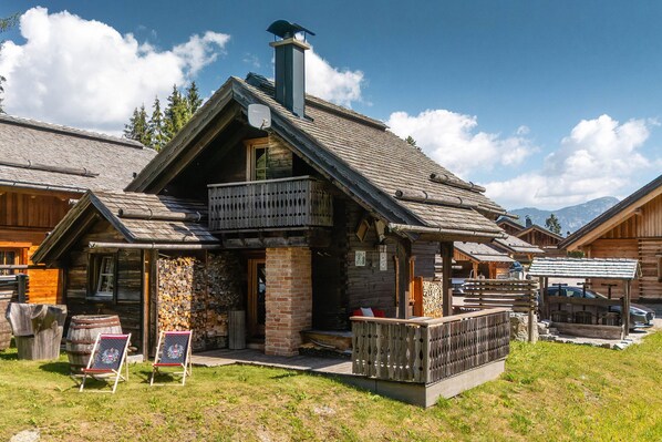 A rustic wooden building with a sloped roof, a chimney, and a balcony.