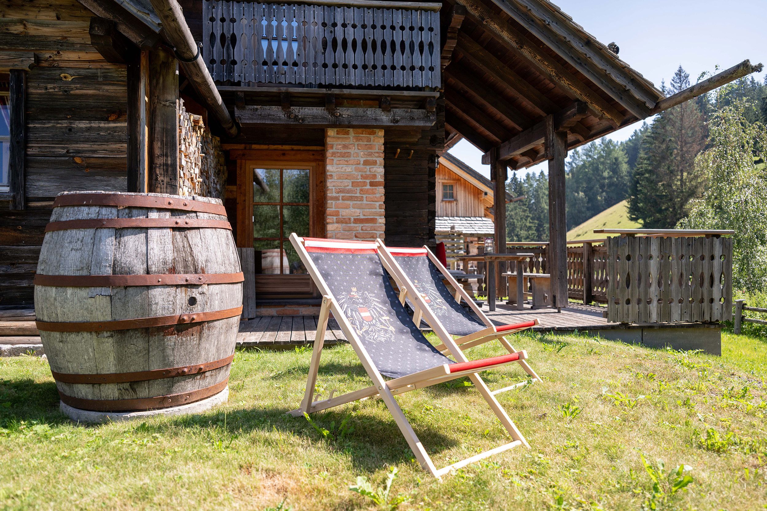 Eine rustikale Holzhütte mit Balkon, einem großen Fass und zwei Strandstühlen.
