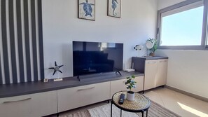 Moderni olohuone, jossa on litteänäyttöinen televisio, meritähtikoriste, pieni pyöreä pöytä, jossa on kasvi, ja ikkuna, josta on näkymä.