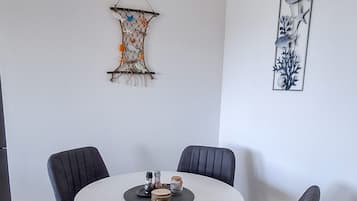 Ruokailutila, jossa on pyöreä pöytä ja neljä tuolia, seinälle kiinnitetty koriste-esine ja kehystetty taideteos.