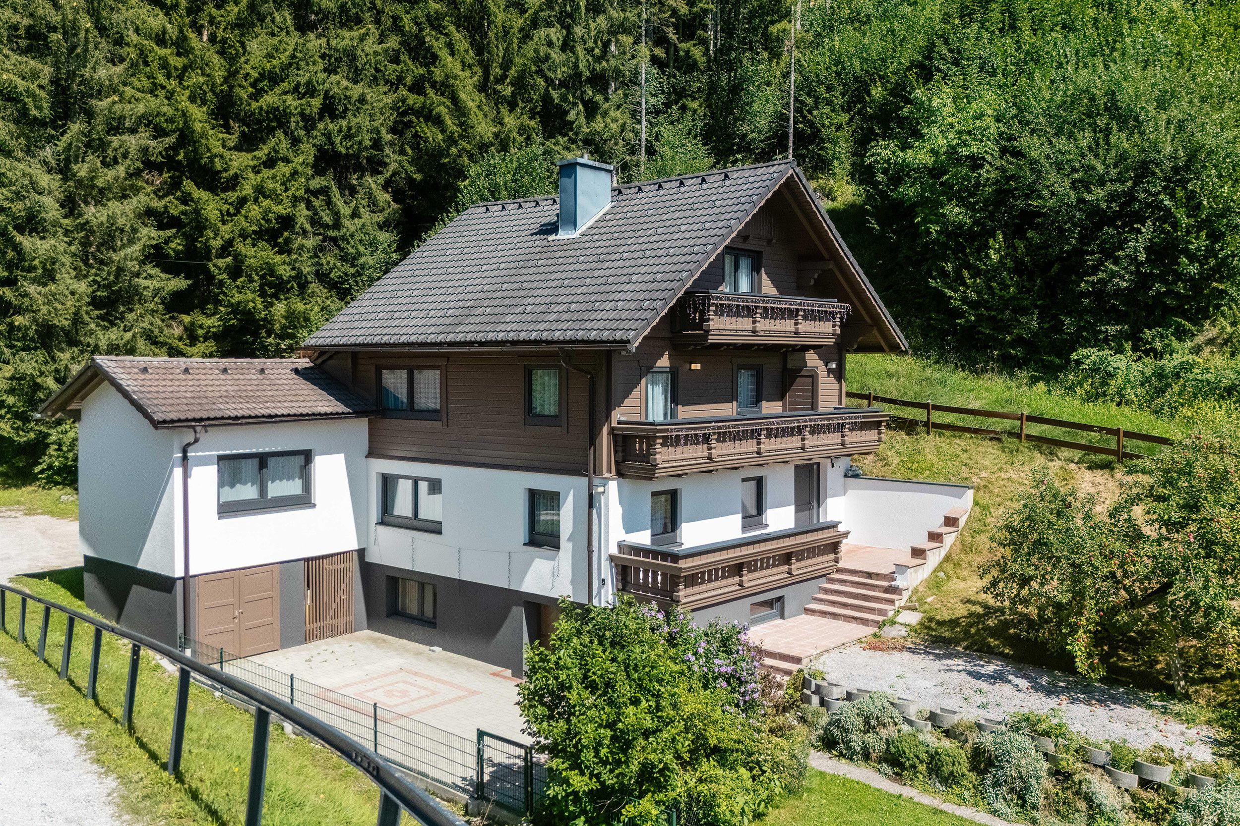 A two-story house with a balcony, surrounded by greenery.