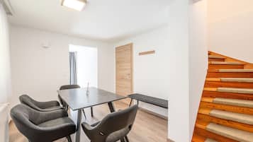 A modern interior with a dining table, four chairs, a bench, a wooden door, and a wooden staircase.