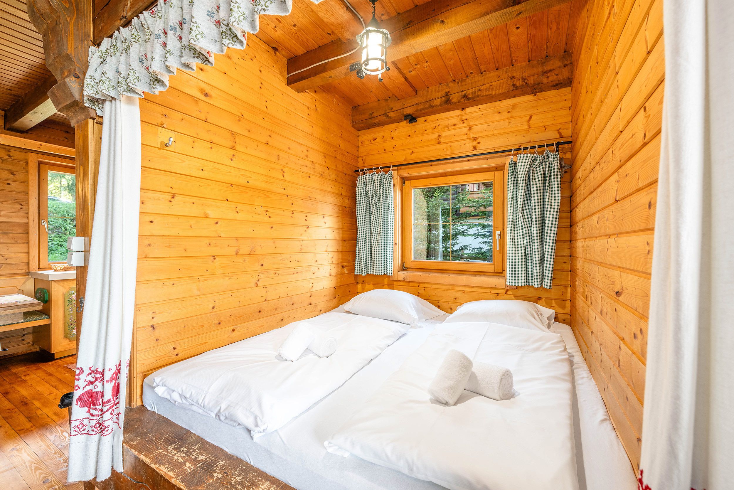 Une pièce de cabane en bois comprenant un lit, une fenêtre avec des rideaux et un plafond en bois.