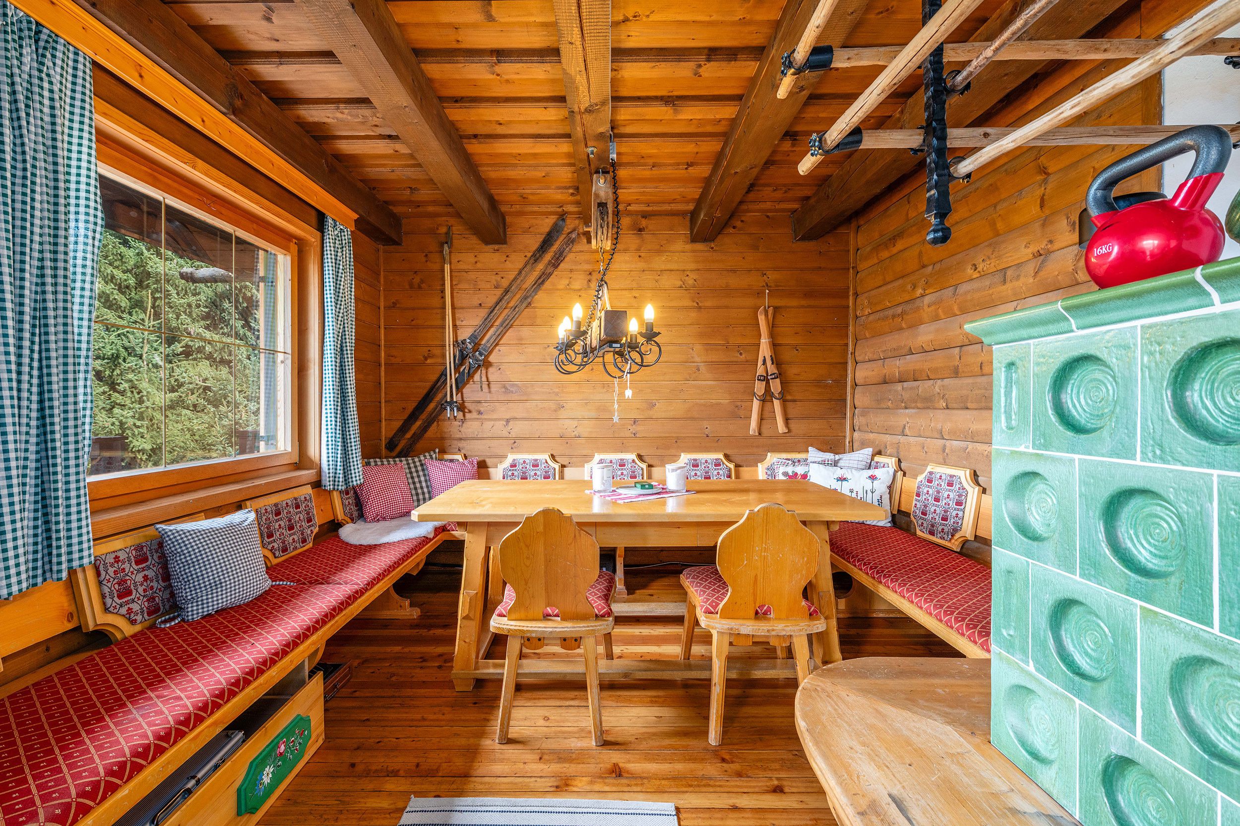 Interior de una cabaña de madera con una mesa de comedor, bancos y un armario verde.
