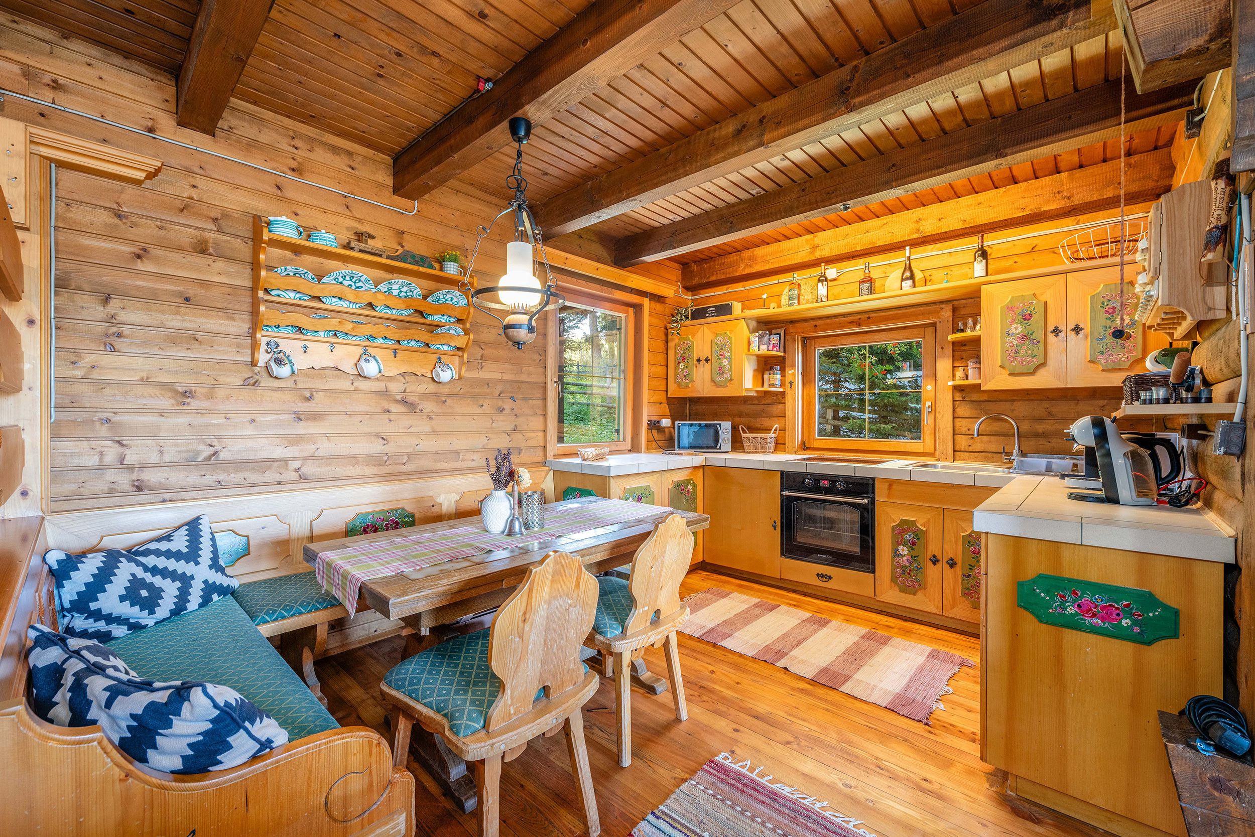A cozy cabin interior with a wooden dining area, a kitchen with wooden cabinets, and a large window providing a view of the outdoors.