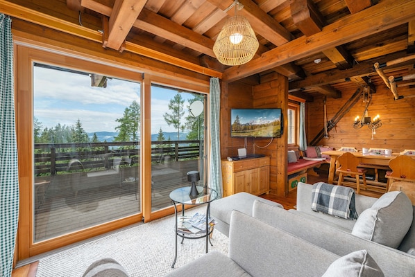 A cozy cabin interior with a large sliding glass door, a sofa, a dining area, and a television.