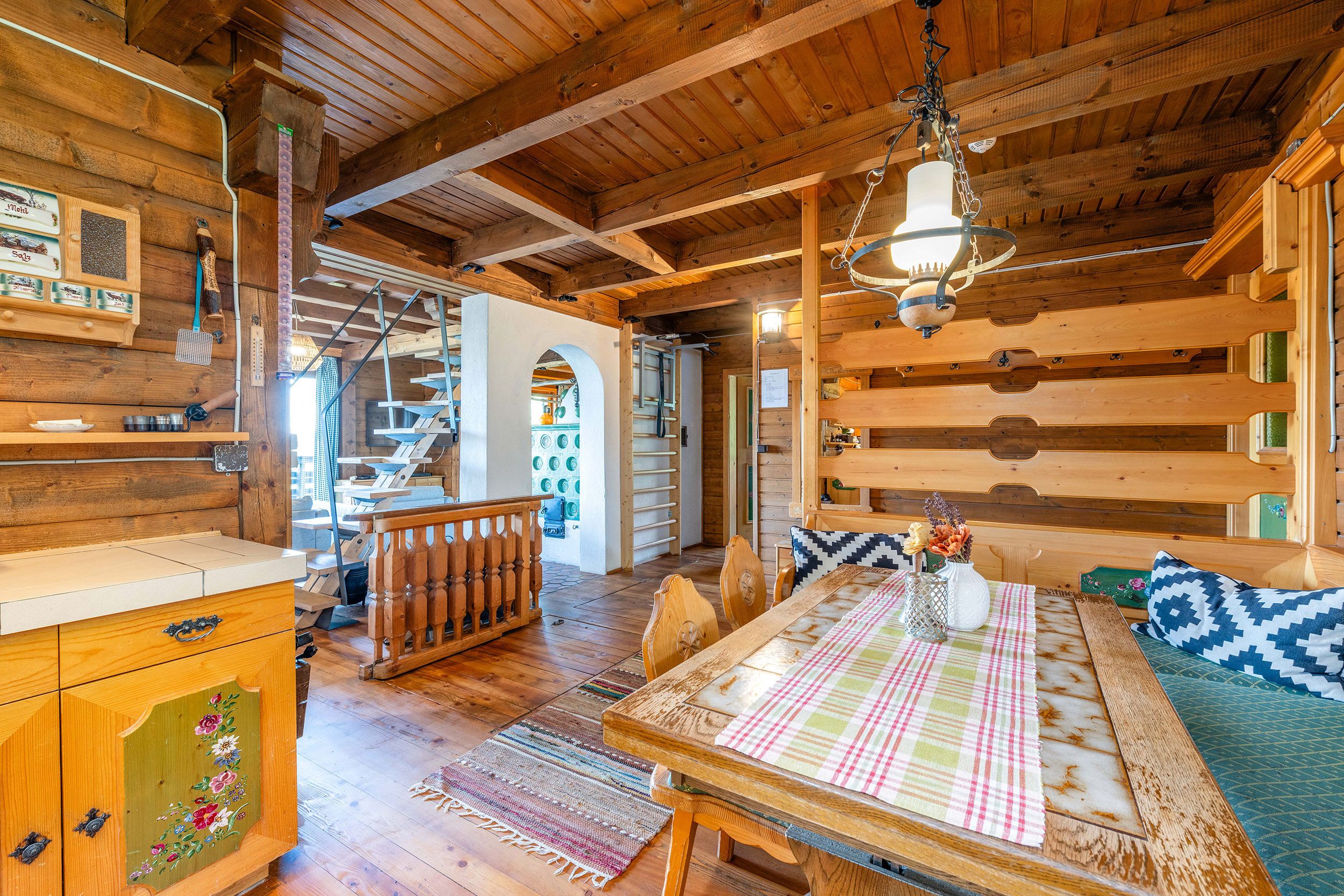 Ein gemütliches Blockhaus-Interieur mit einem Holzesstisch, einer Bank und einer Treppe, die zu einer oberen Ebene führt.