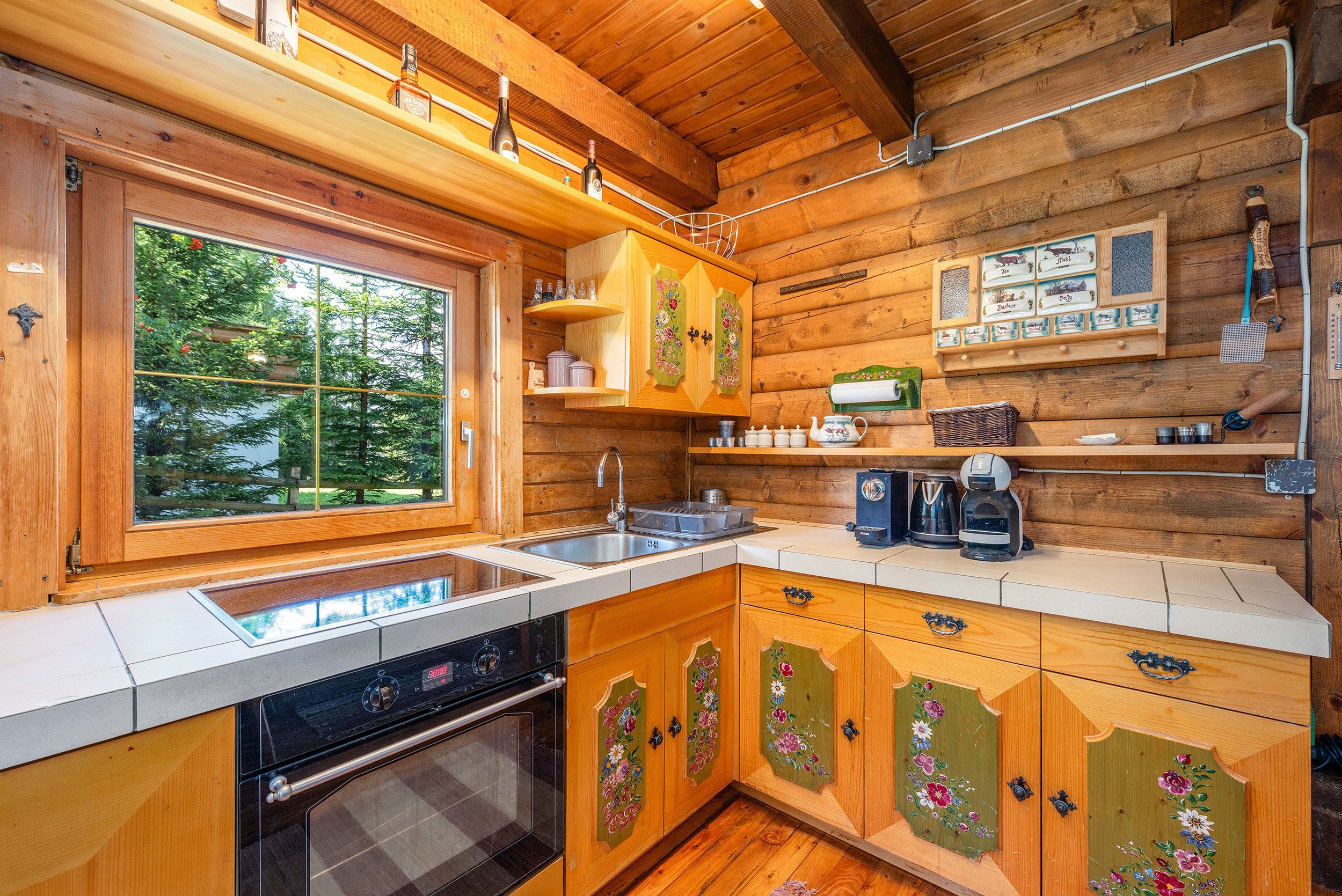 Eine Holzhütte mit einer Küche, inklusive Backofen, Spüle und einem Fenster mit Blick auf Grünflächen.