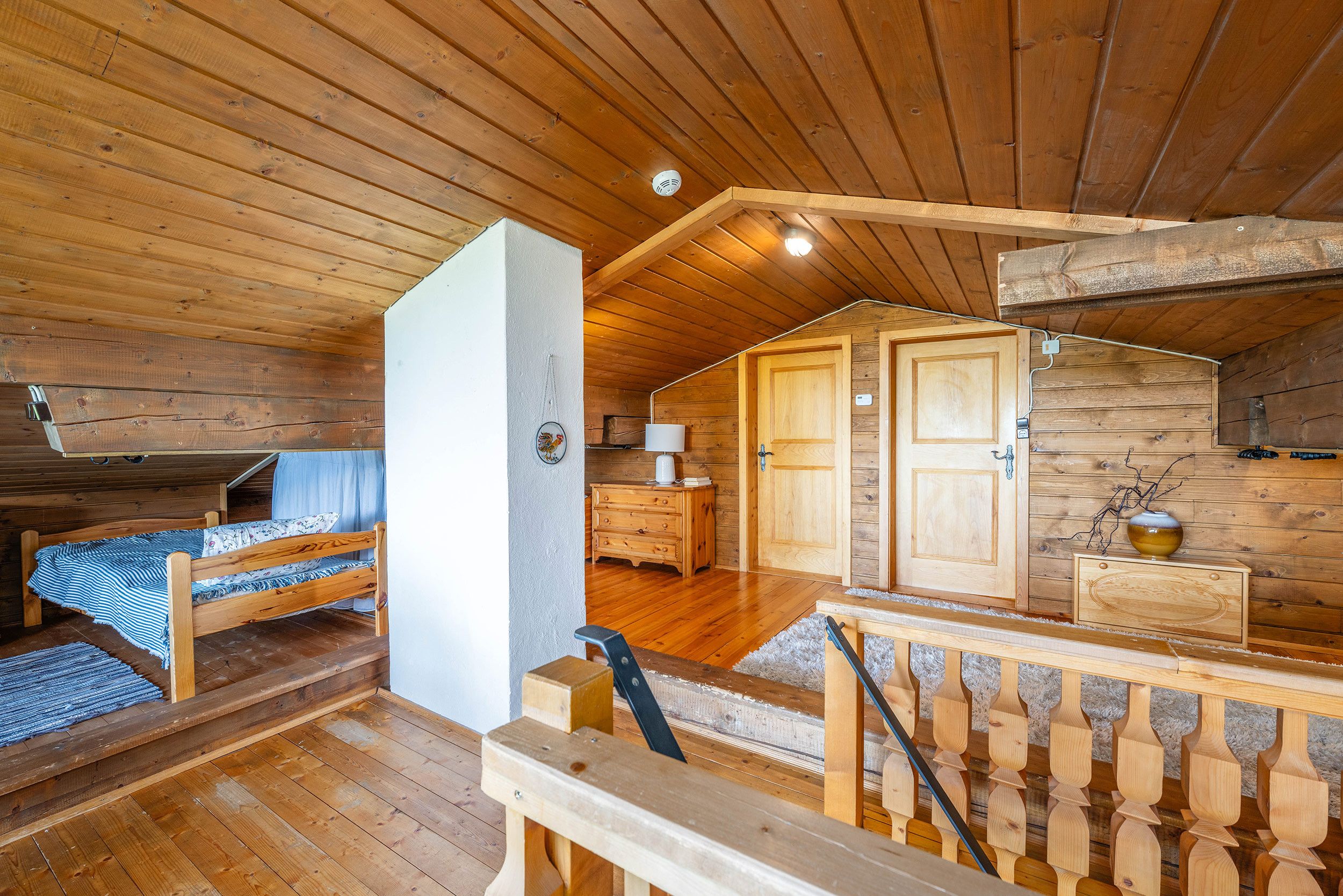 Ein Holzblockhaus-Innenraum mit Etagenbett, Schreibtisch, Kommode und einer Tür zu einem anderen Raum.