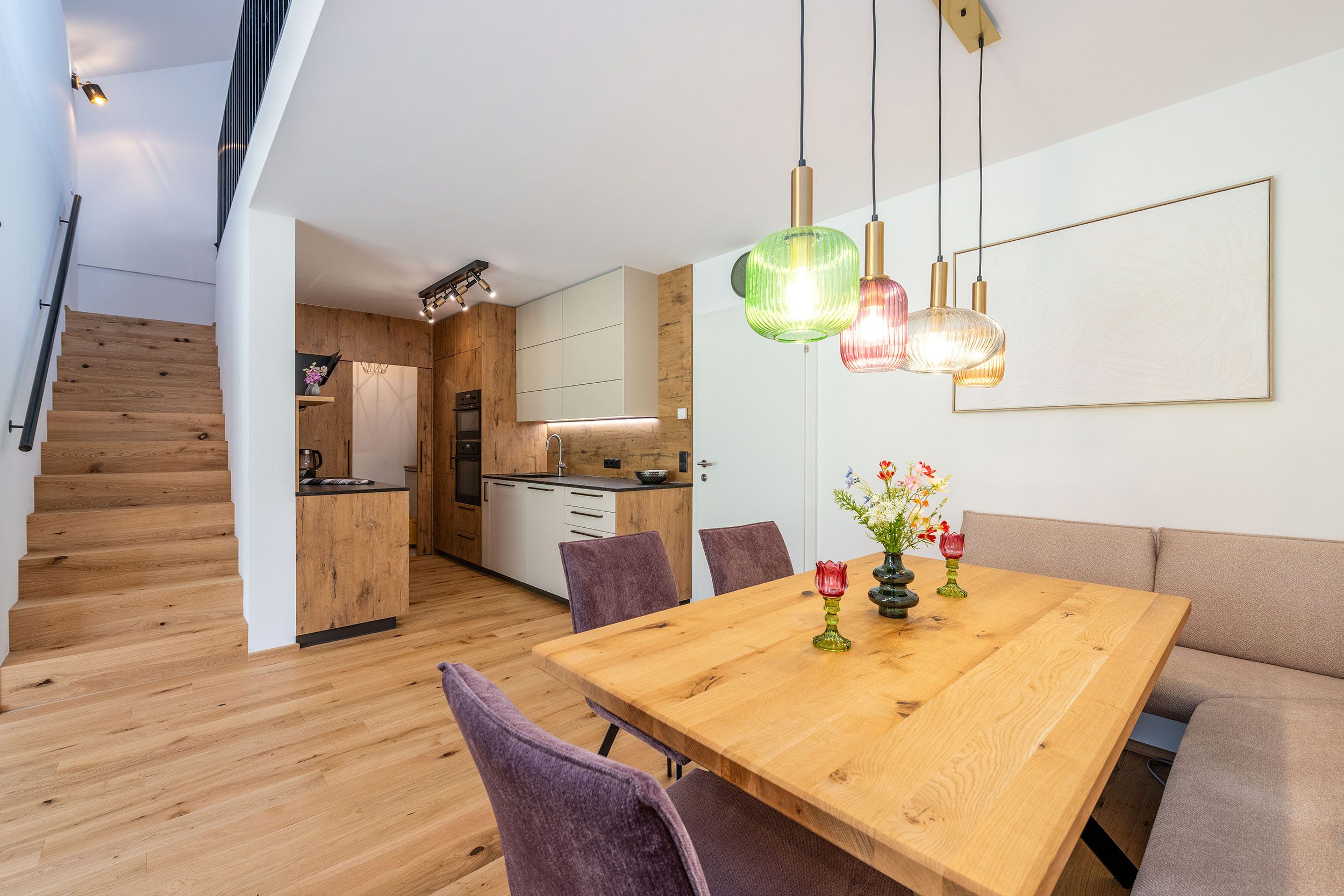 Une cuisine moderne avec des meubles en bois, un coin repas doté d’une table en bois et un escalier.