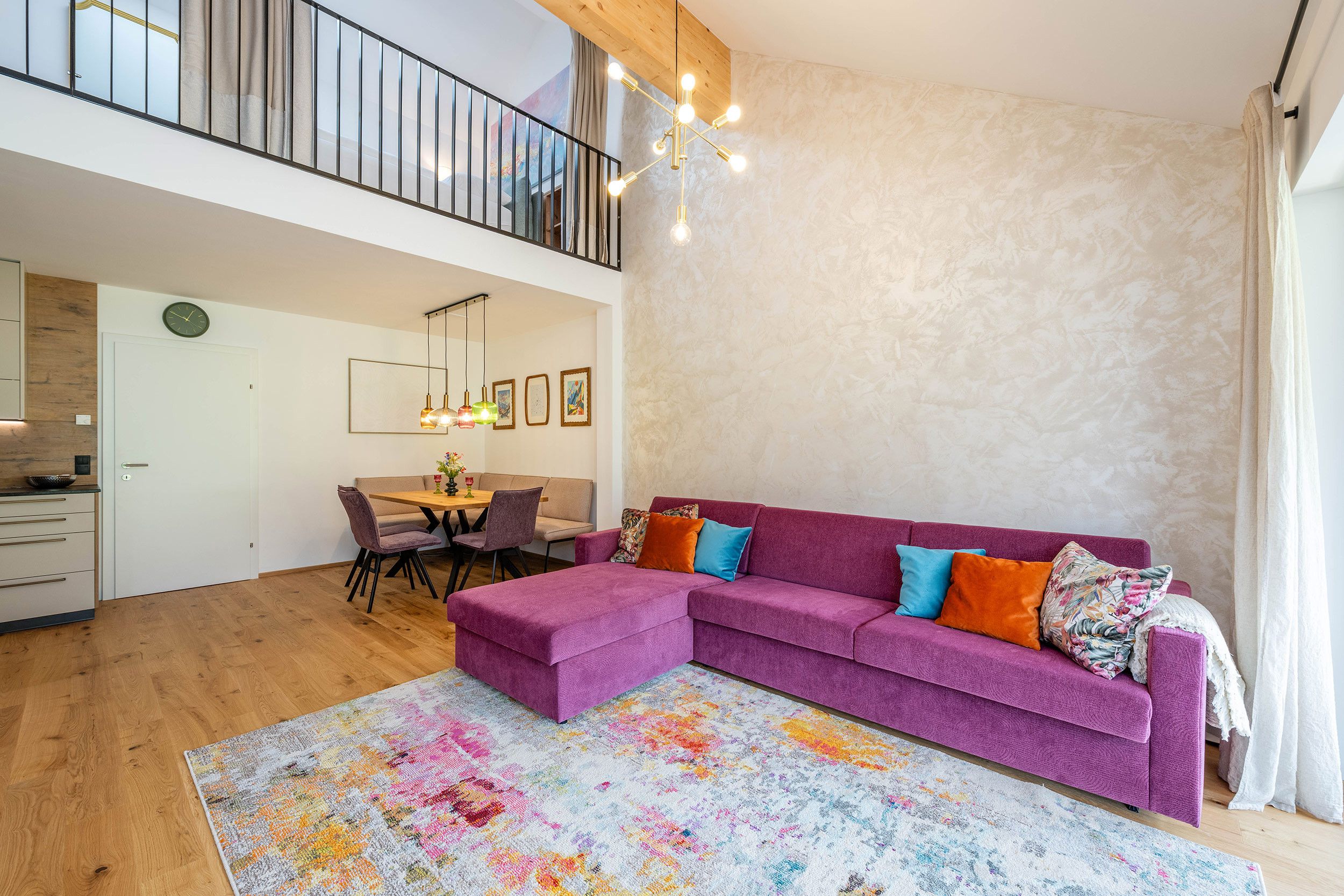 Un vaste espace de vie comprenant un canapé violet, une table à manger et un escalier menant à un niveau supérieur.