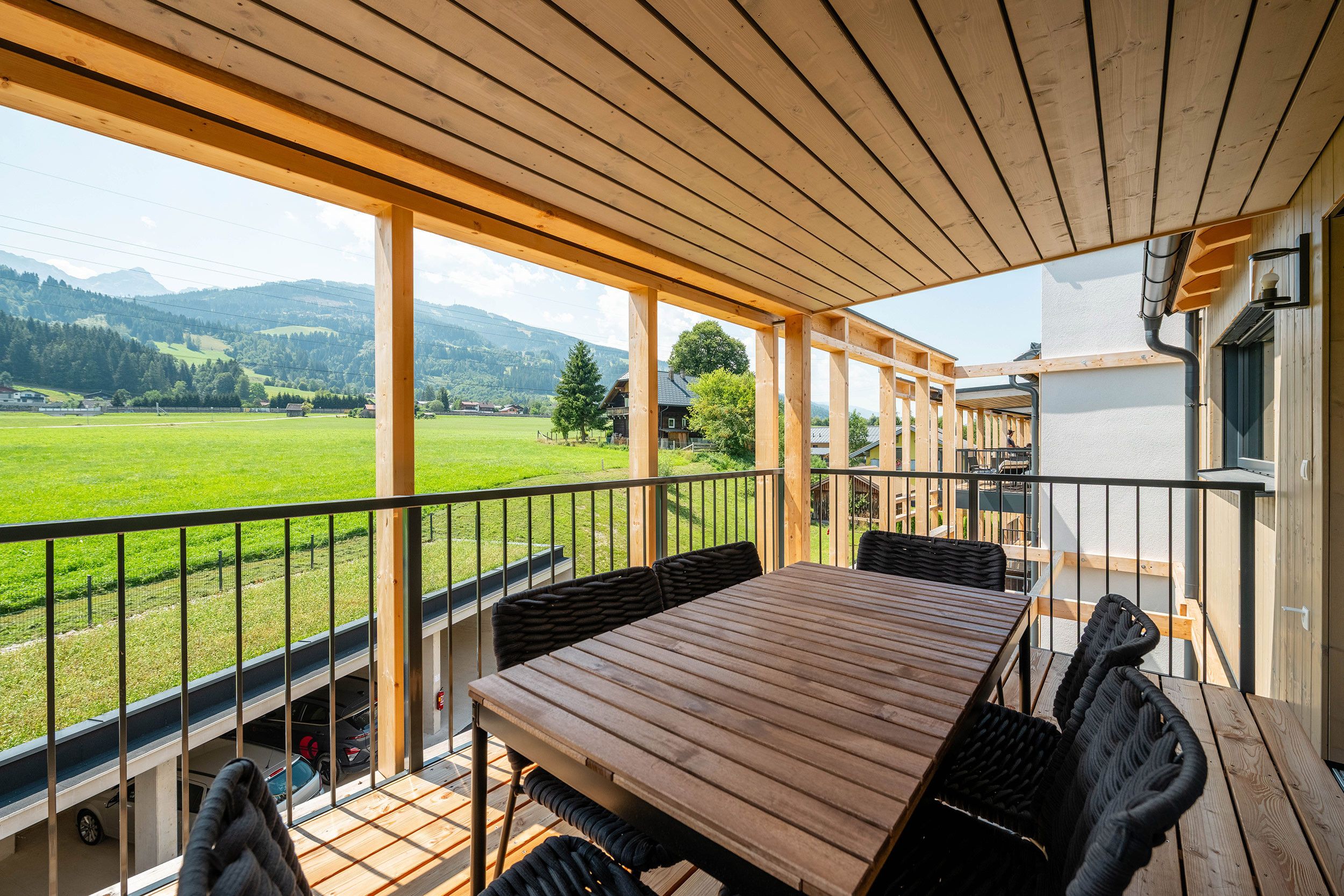 Eine Holzterrasse mit Tisch und Stühlen, mit Blick auf eine grüne Landschaft mit Bergen.