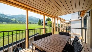 Eine Holzterrasse mit Tisch und Stühlen, mit Blick auf eine grüne Landschaft mit Bergen.