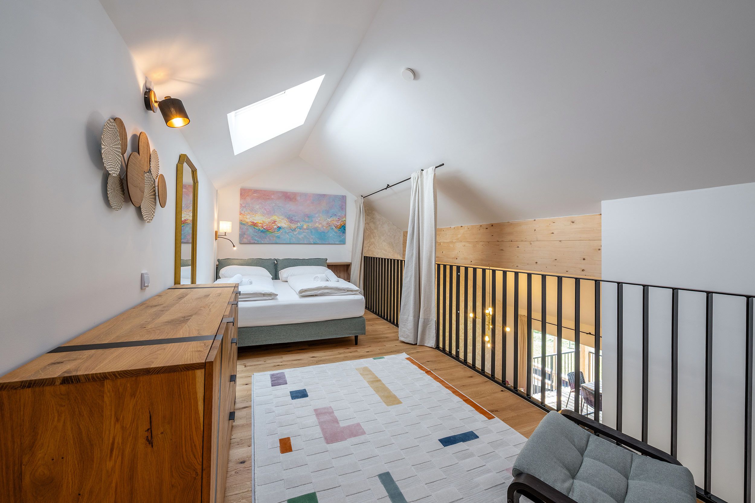 Ein Schlafzimmer mit einem Bett, einem Holztisch, einem Gemälde und Blick ins Freie.