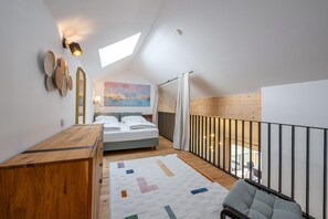 Ein Schlafzimmer mit einem Bett, einem Holztisch, einem Gemälde und Blick ins Freie.