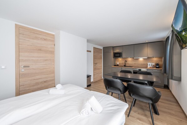 Ein modernes Hotelzimmer mit Bett, einer kleinen Küchenzeile und einem Esstisch.